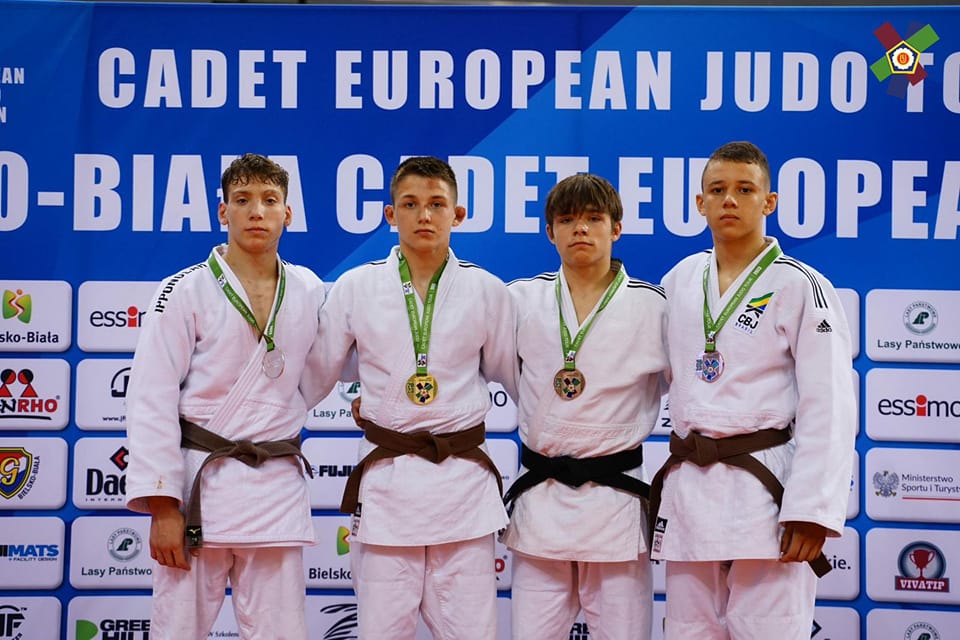 Czterech młodych zawodników w białych judogach z medalami na szyjach stojących na tle niebieskiej ścianki z napisem Cadet European judo i logotypami sponsorów i partnerów.